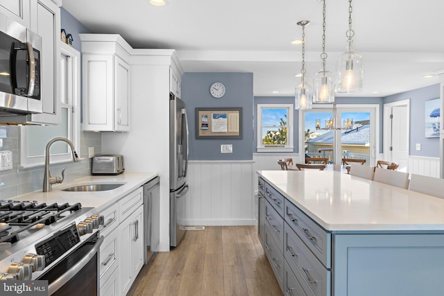 kitchen featuring white cabinetry, sink, stainless steel appliances, light hardwood / wood-style floors, and pendant lighting