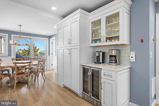 kitchen with backsplash, pendant lighting, white cabinets, light hardwood / wood-style floors, and wine cooler