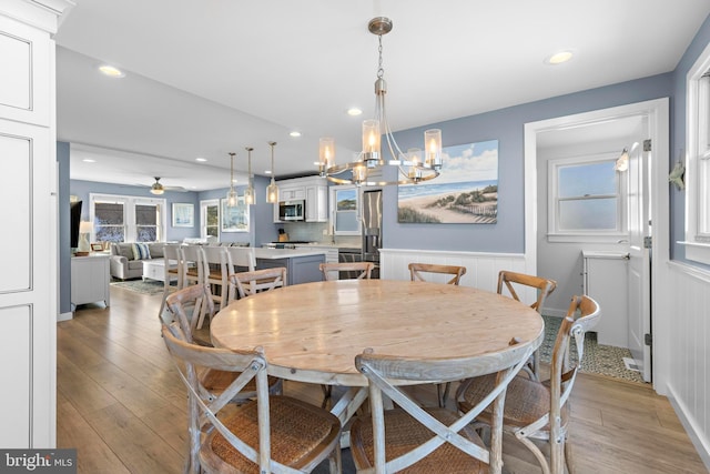 dining area with ceiling fan with notable chandelier and light hardwood / wood-style floors