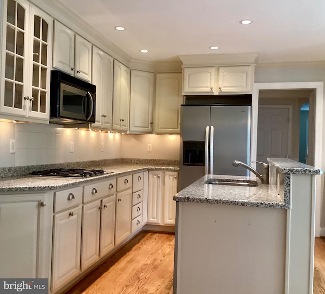 kitchen with white cabinetry, appliances with stainless steel finishes, light stone countertops, sink, and light hardwood / wood-style flooring