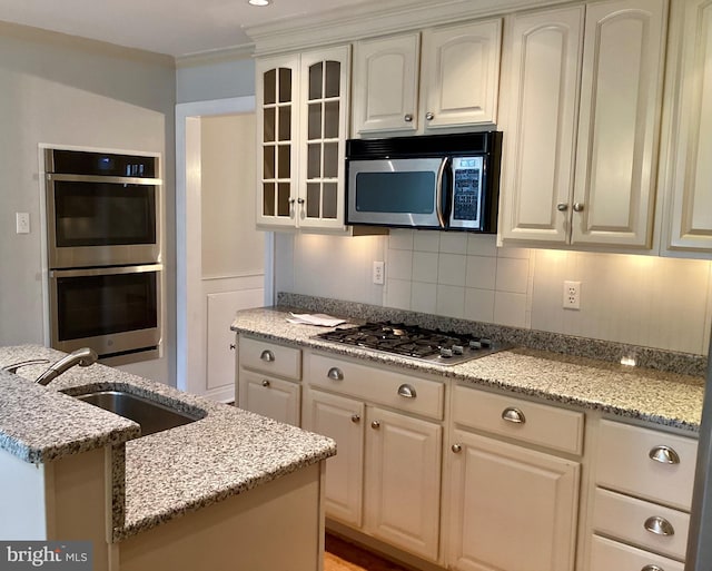 kitchen with appliances with stainless steel finishes, ornamental molding, light stone counters, white cabinets, and sink