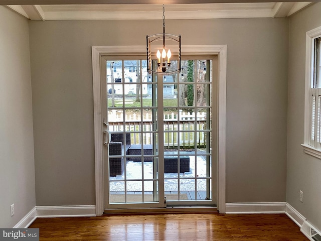 doorway with an inviting chandelier, crown molding, and wood-type flooring