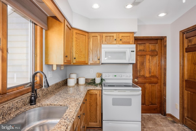 kitchen with baseboards, light stone counters, recessed lighting, white appliances, and a sink