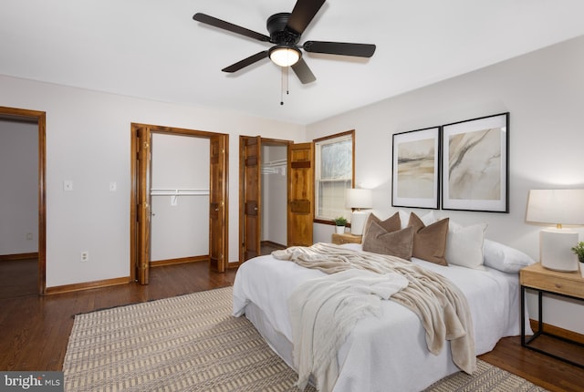 bedroom with wood finished floors, baseboards, two closets, and ceiling fan