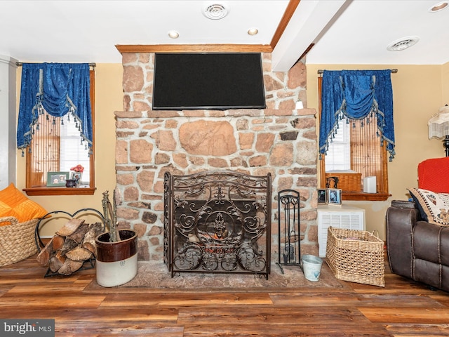 living room with hardwood / wood-style flooring, a stone fireplace, and beam ceiling