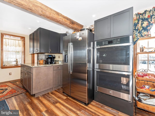 kitchen featuring light stone counters, a wealth of natural light, beamed ceiling, and appliances with stainless steel finishes