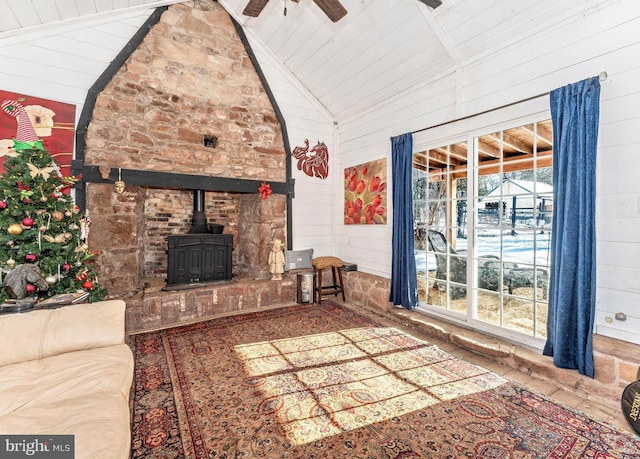 unfurnished living room featuring high vaulted ceiling, wood walls, ceiling fan, and a wood stove