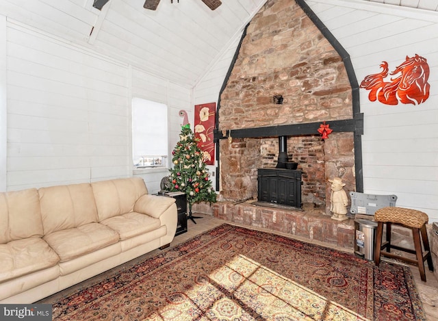 living room featuring high vaulted ceiling, a wood stove, ceiling fan, and wood walls