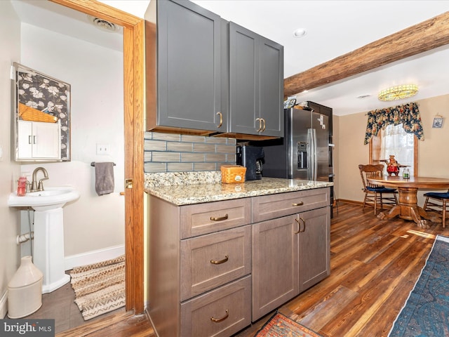 kitchen with stainless steel refrigerator with ice dispenser, light stone counters, dark hardwood / wood-style flooring, gray cabinets, and decorative backsplash