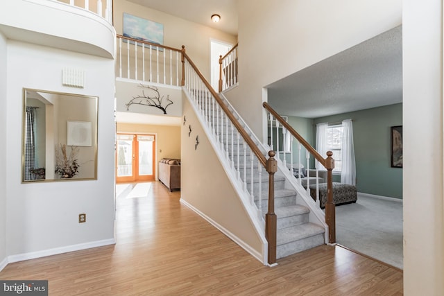 stairs with french doors, a high ceiling, and hardwood / wood-style flooring