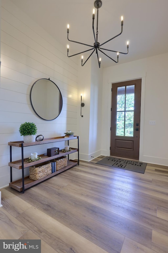 entryway with a chandelier, wooden walls, and light hardwood / wood-style flooring