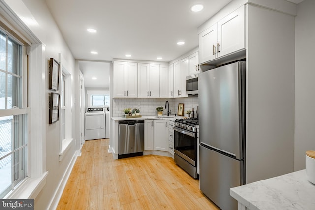 kitchen featuring washing machine and clothes dryer, white cabinetry, tasteful backsplash, and appliances with stainless steel finishes