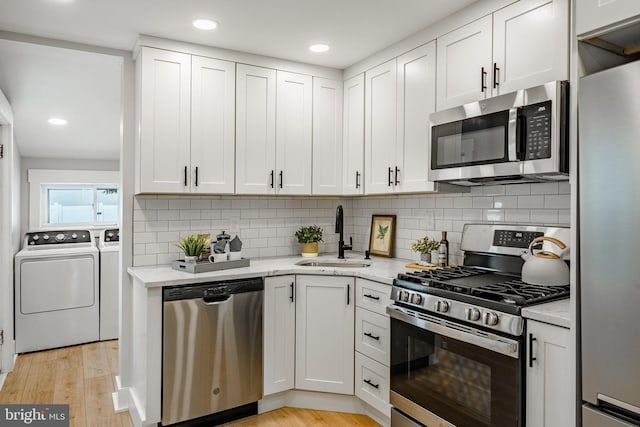 kitchen featuring light stone countertops, appliances with stainless steel finishes, sink, washing machine and clothes dryer, and white cabinets