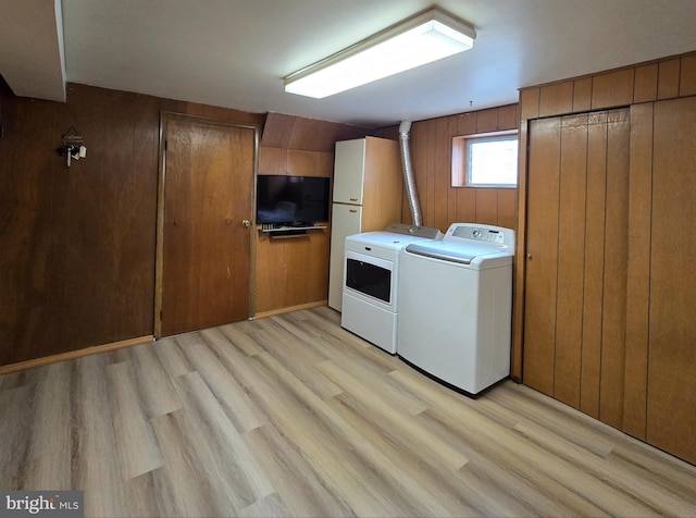 laundry area featuring separate washer and dryer, light hardwood / wood-style floors, and wood walls