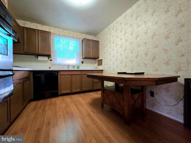 kitchen with black dishwasher, sink, oven, and light hardwood / wood-style flooring