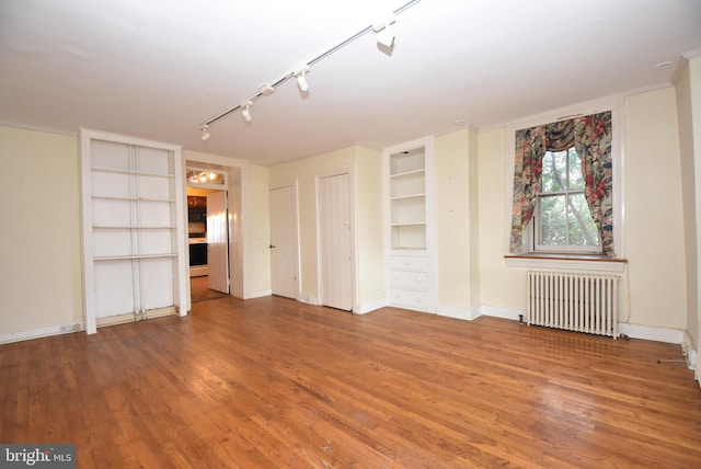 interior space with radiator heating unit, rail lighting, built in features, and wood-type flooring