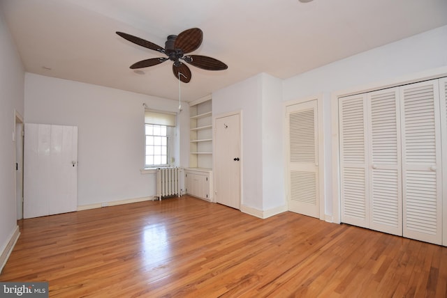 unfurnished bedroom featuring ceiling fan, light wood-type flooring, radiator heating unit, and multiple closets