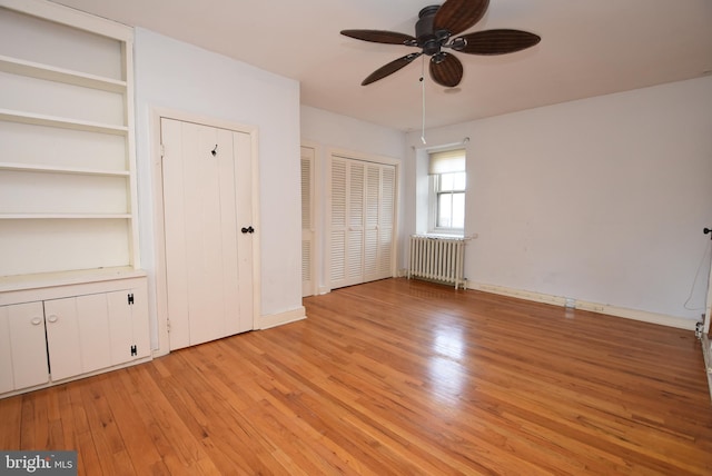 unfurnished bedroom featuring radiator heating unit, two closets, light hardwood / wood-style flooring, and ceiling fan