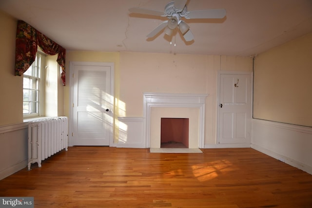 unfurnished living room with ceiling fan, radiator heating unit, and light wood-type flooring