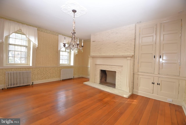 unfurnished living room with hardwood / wood-style flooring, a notable chandelier, a fireplace, and radiator