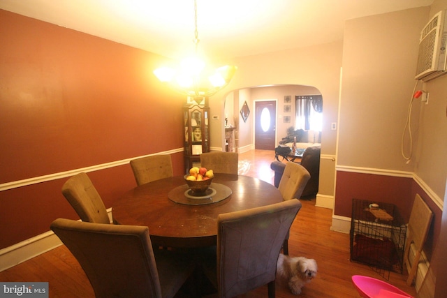 dining room featuring a wall mounted air conditioner, a notable chandelier, and wood-type flooring