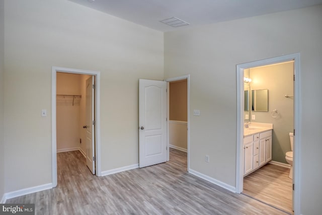 unfurnished bedroom featuring a spacious closet, light hardwood / wood-style floors, a closet, and ensuite bathroom