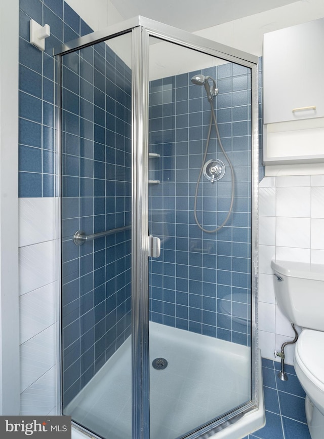 bathroom with tile patterned floors, toilet, tile walls, and a shower with shower door