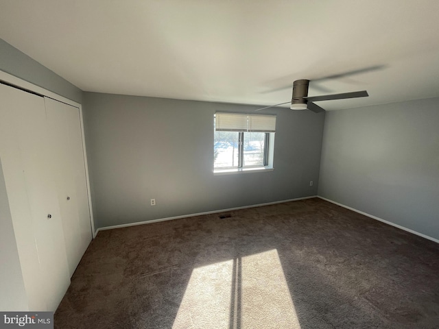 unfurnished bedroom featuring ceiling fan, dark carpet, and a closet