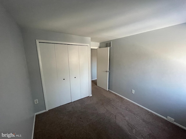 unfurnished bedroom with dark carpet and a closet