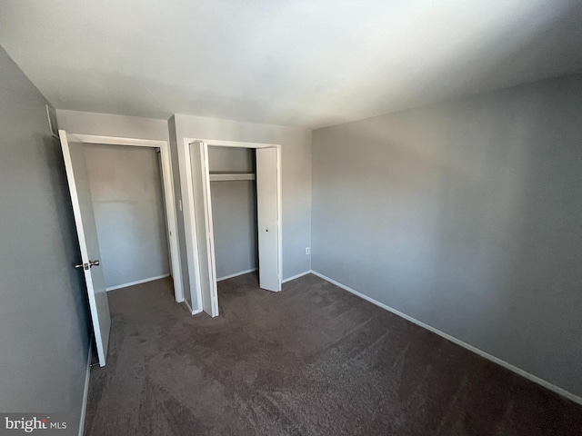 unfurnished bedroom featuring dark carpet and two closets