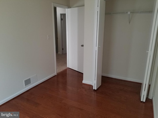 unfurnished bedroom with a closet, wood finished floors, visible vents, and baseboards