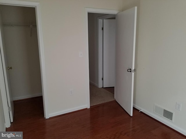 unfurnished bedroom with a closet, visible vents, baseboards, and wood finished floors