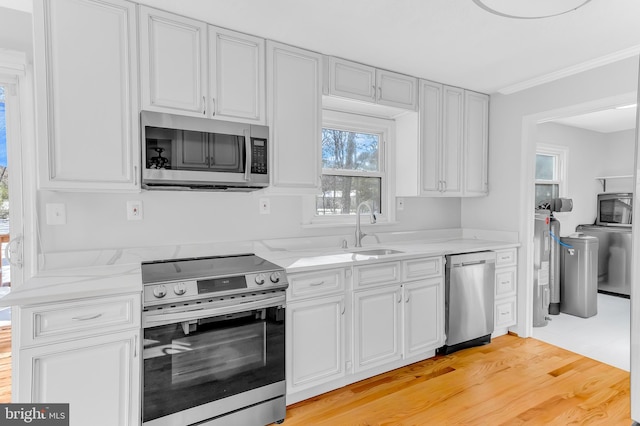 kitchen featuring sink, crown molding, light wood-type flooring, light stone countertops, and stainless steel appliances