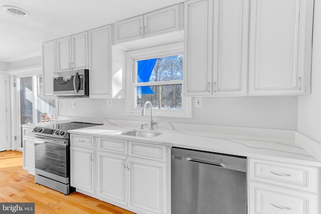 kitchen featuring sink, light stone counters, stainless steel appliances, and light hardwood / wood-style floors