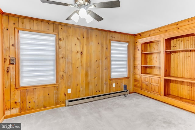 carpeted empty room with ceiling fan, a wealth of natural light, a baseboard heating unit, and wooden walls