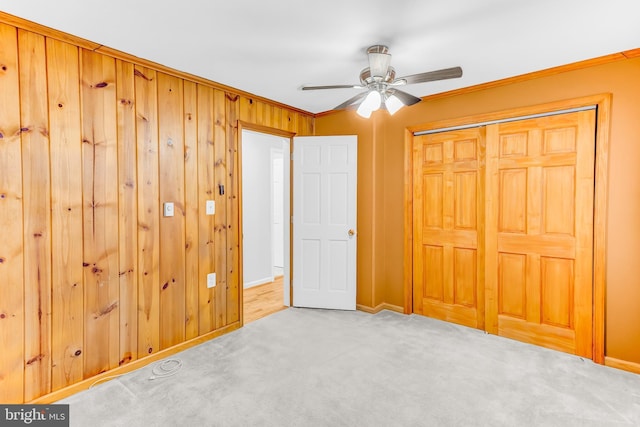 unfurnished bedroom featuring ceiling fan, carpet, wooden walls, crown molding, and a closet