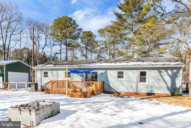 snow covered rear of property featuring an outbuilding, a deck, and a garage