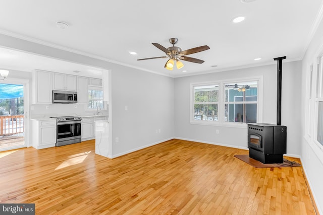 unfurnished living room featuring plenty of natural light, crown molding, a wood stove, and light hardwood / wood-style floors