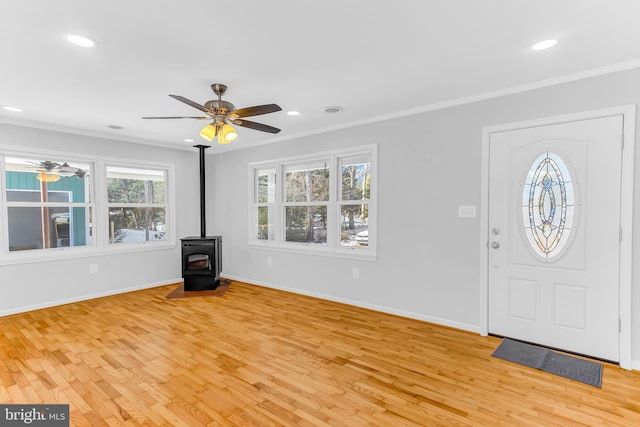 foyer entrance featuring ceiling fan, a wood stove, ornamental molding, and light wood-type flooring