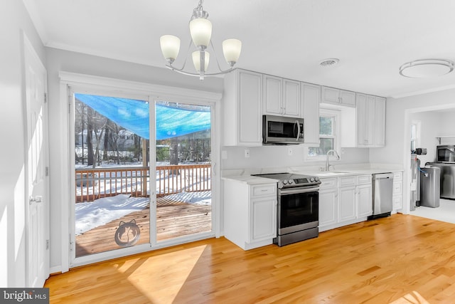 kitchen featuring appliances with stainless steel finishes, decorative light fixtures, sink, a notable chandelier, and light wood-type flooring