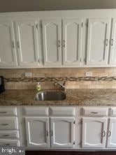 details with dark stone countertops, white cabinetry, sink, and tasteful backsplash