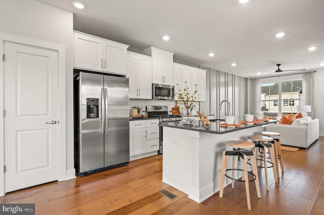 kitchen with a kitchen island with sink, white cabinets, ceiling fan, appliances with stainless steel finishes, and a kitchen bar