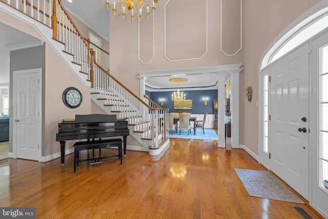 foyer with wood-type flooring, an inviting chandelier, ornamental molding, and ornate columns