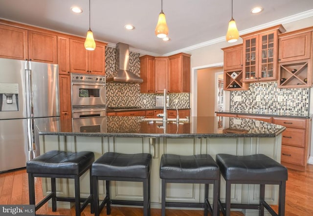 kitchen with decorative backsplash, a kitchen breakfast bar, wall chimney range hood, an island with sink, and stainless steel appliances