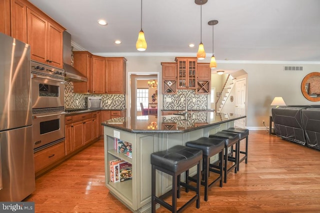 kitchen with pendant lighting, stainless steel appliances, a kitchen breakfast bar, light wood-type flooring, and a center island with sink