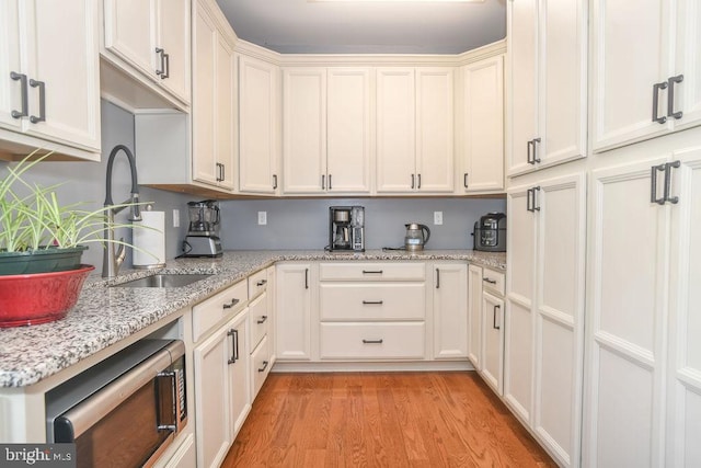 kitchen featuring light wood-type flooring, light stone counters, and sink