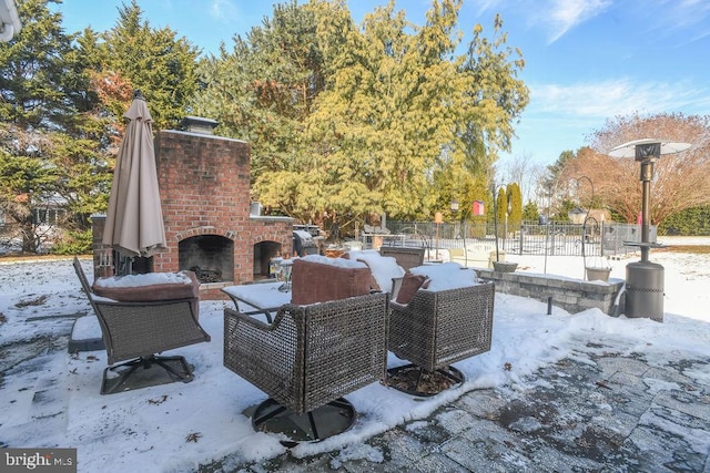 snow covered patio featuring an outdoor brick fireplace