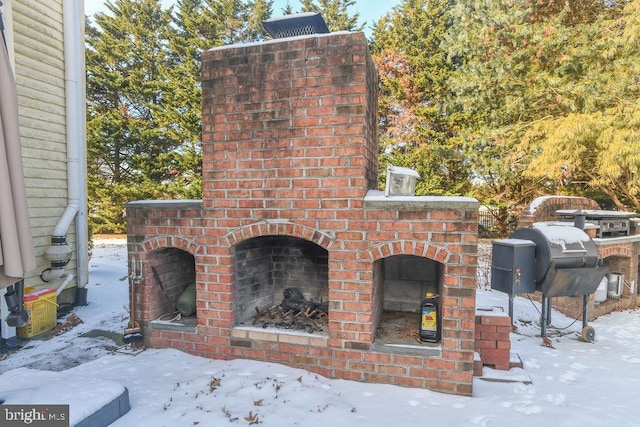 snow covered patio featuring grilling area and an outdoor brick fireplace