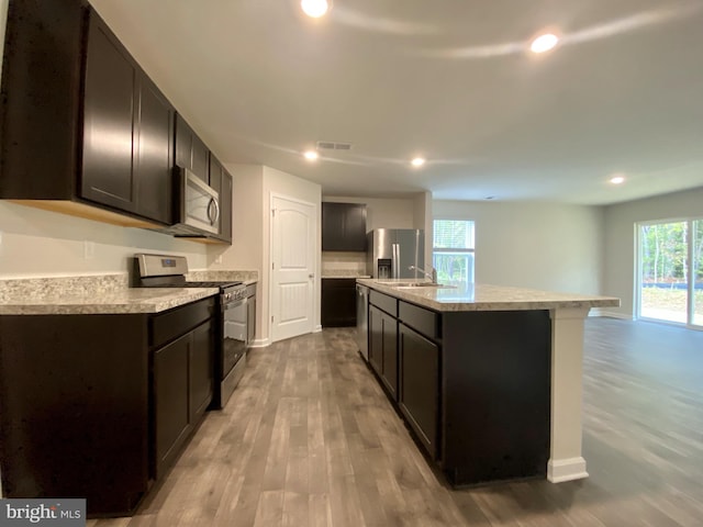 kitchen with a healthy amount of sunlight, a kitchen island with sink, stainless steel appliances, and light hardwood / wood-style floors