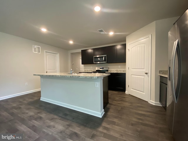 kitchen with appliances with stainless steel finishes, light stone counters, sink, dark hardwood / wood-style floors, and an island with sink